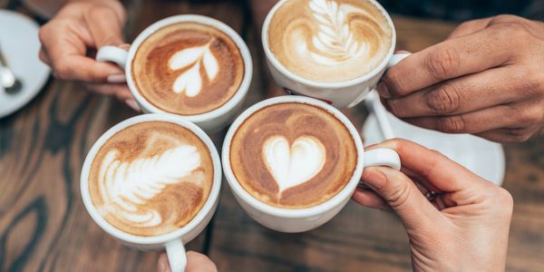 Four hands holding cappuccinos with latte art, toasting together.