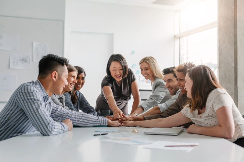 Korean mature businesswoman leads multiracial group of work colleagues in team building and agreement positive emotion in brainstorming planning session together in modern office meeting daytime