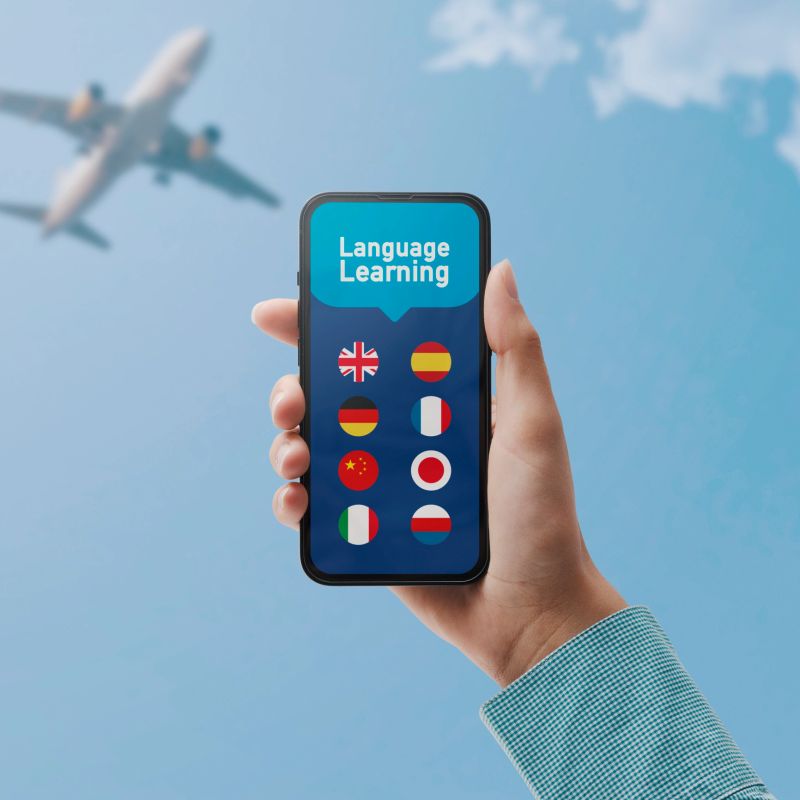 Learn languages online: hand holding a smartphone with language learning app and set of flags