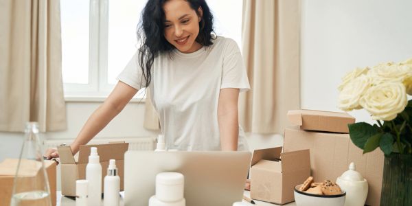 Woman working on her laptop surrounded by skincare products and packaging.