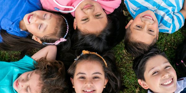 Children lying on grass in a circle, smiling and relaxing.