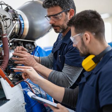 Two engineers inspecting and testing aircraft machinery with safety gear.