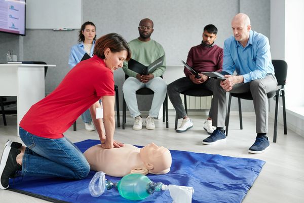 Woman practicing CPR on a manikin with group observing.