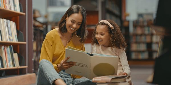 Woman reading a book to a young girl in a library.