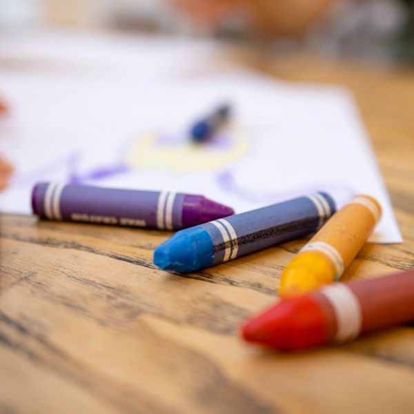 Close-up of colorful crayons on a wooden surface with a drawing in the background.