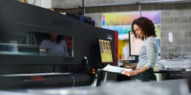 A woman operating a large industrial printer in a print shop.