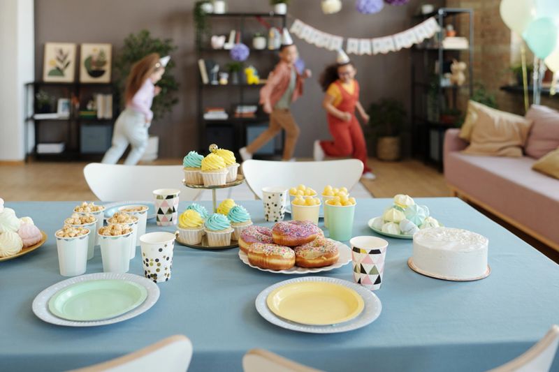 Horizontal image of candy bar on table with donuts, cupcakes and popcorn with group of children running in background