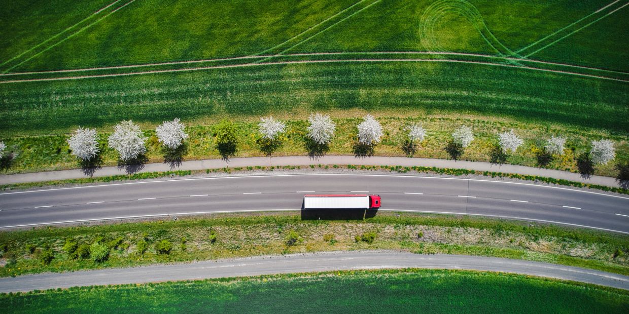 A red truck on a curved road with green fields.