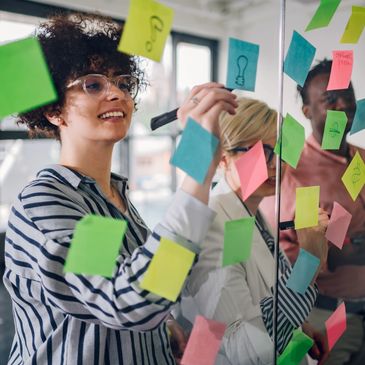 Creative professionals planning website strategy with sticky notes on glass board.