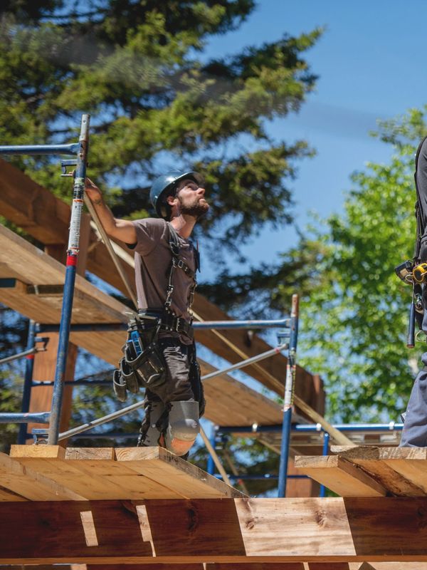 Three construction workers installing wooden beams outdoors on a sunny day.