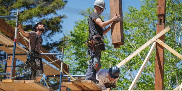Three construction workers installing wooden beams outdoors on a sunny day.