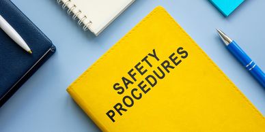 Yellow book titled Safety Procedures with pens and notebooks on a blue surface.