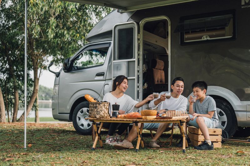 Happy Asian parents and their kid communicating while spending a spring day on camping. - Camper van travel series