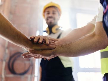 Construction workers stacking hands in a teamwork gesture.
