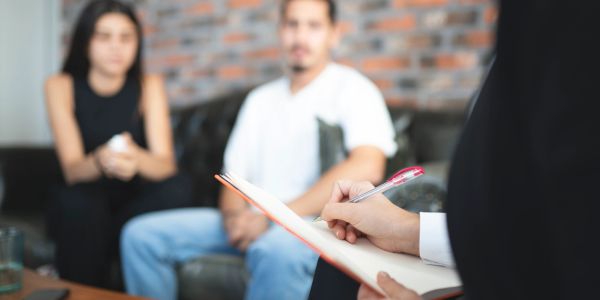 Couple talking with a therapist taking notes.