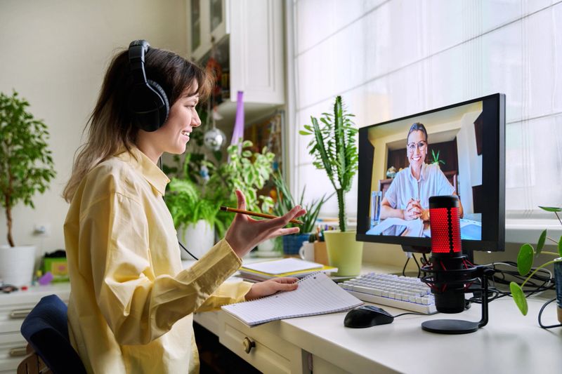Teenage female student studying online at home, female in headphones with notebook talking to teacher by video, using computer. Chat call conference, e-learning college high school, technology concept