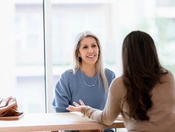 Two women engaged in a friendly conversation at a table indoors.