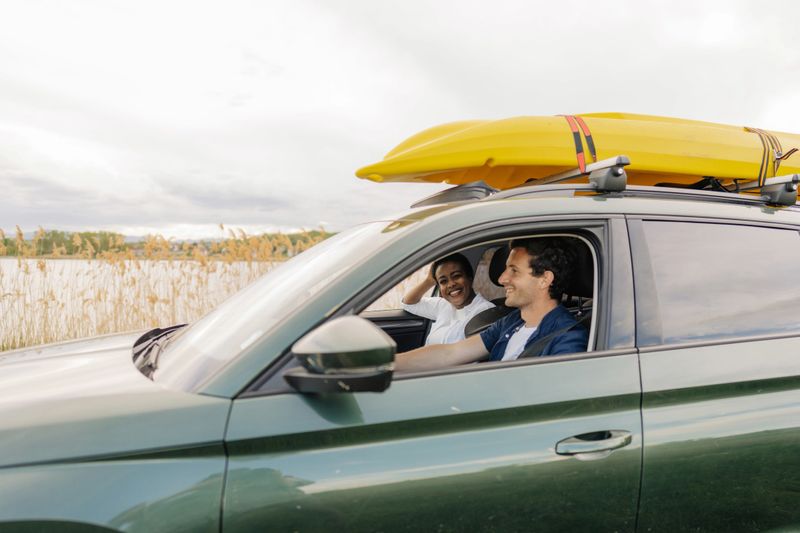 Photo of a smiling couple on the way to the lake. The kayak is on the roof of the car.