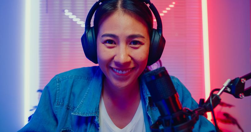 Close up of young Asian woman playing online computer video game and broadcast streaming live in neon lights living room at home. Gamer lifestyle concept.