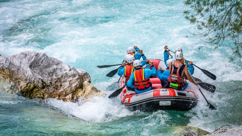 Rear view of friends wearing life jacket and rafting in river.