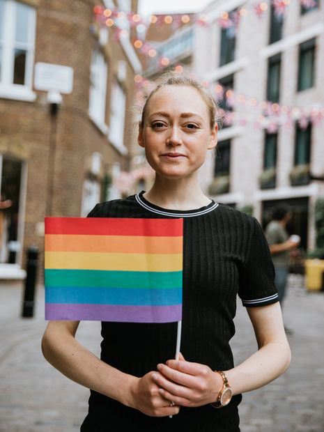 Person holding a rainbow pride flag outdoors in an urban area.