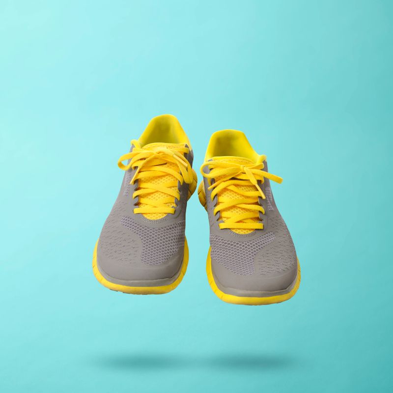 Yellow sneakers walking in mid-air against light blue background with copy space.