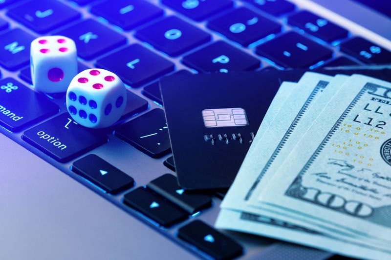 Gambling background. Making profit with online casino, online gaming concept. Game dice, credit card and dollars lie on a modern laptop keypad close-up.