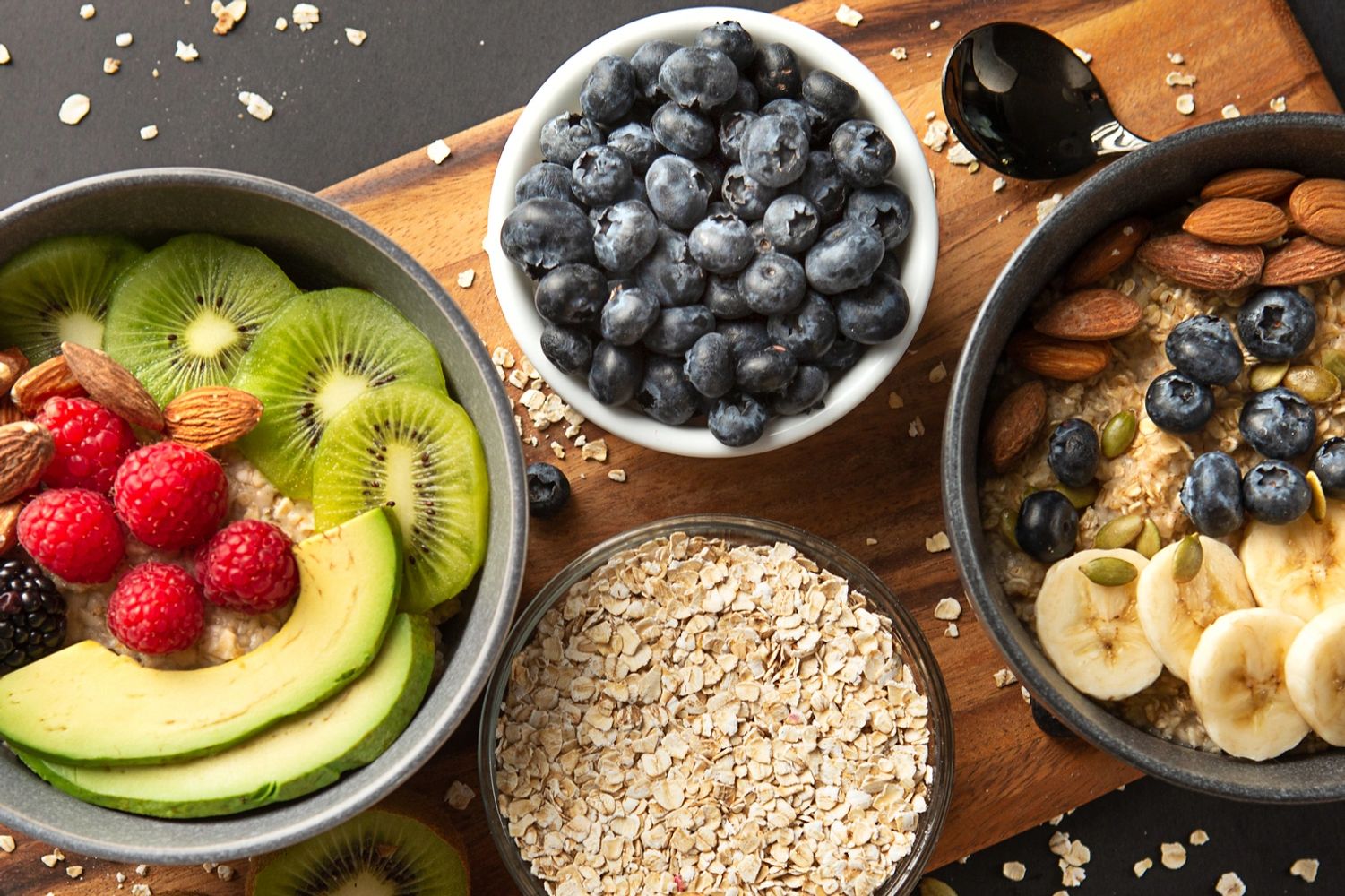 Two bowls of oatmeal topped with fresh fruits and nuts on a wooden board.