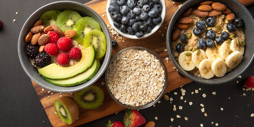 Two fruit and oatmeal bowls with fresh toppings on a dark surface.