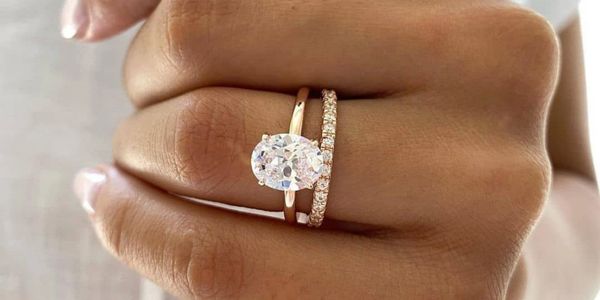 A hand wearing two elegant rings, one with a large oval diamond and one with small diamonds.