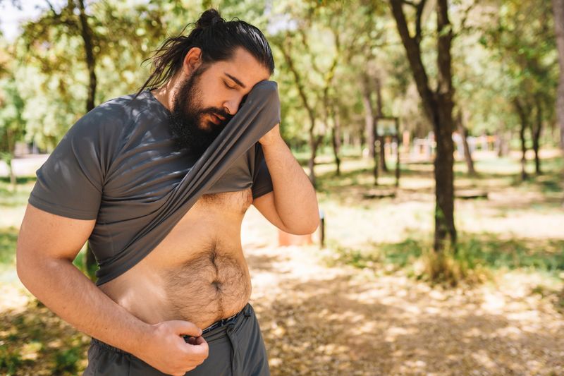 young man practising sport outdoors wiping his sweat with his t-shirt. athlete preparing for a marathon. health and wellness lifestyle. health and wellness lifestyle.outdoor public park, natural sunlight.