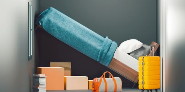 Small room with an angled bed, packed boxes, and bright yellow suitcase.