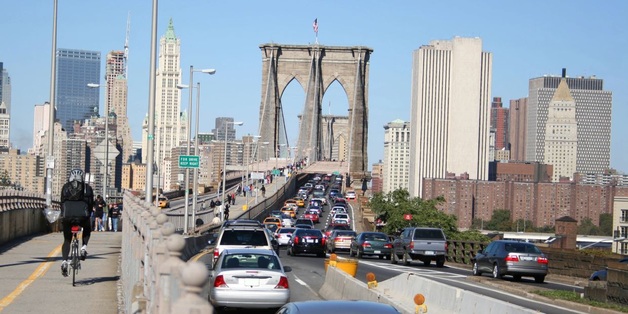 Bicyclist and cars crossing Brooklyn Bridge with city skyline.