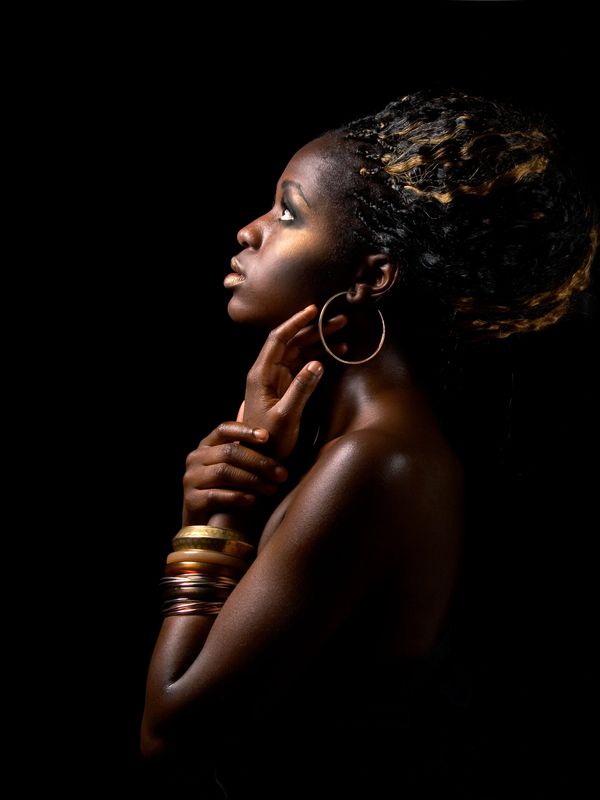 Side profile of woman with hoop earrings and bracelets against black background.