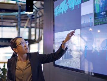 Woman analyzing data on a large interactive screen in a modern office.