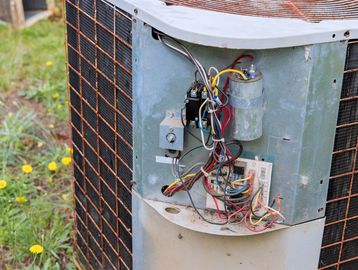 Open outdoor air conditioning unit showing internal wiring and components.