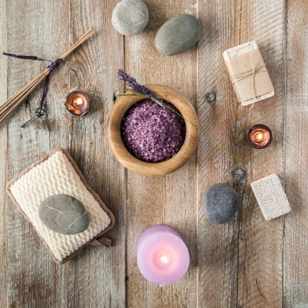 Spa setup with lavender bath salts, candles, and stones on wood.