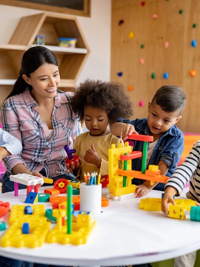 Teacher and diverse children playing with educational toys at a table.