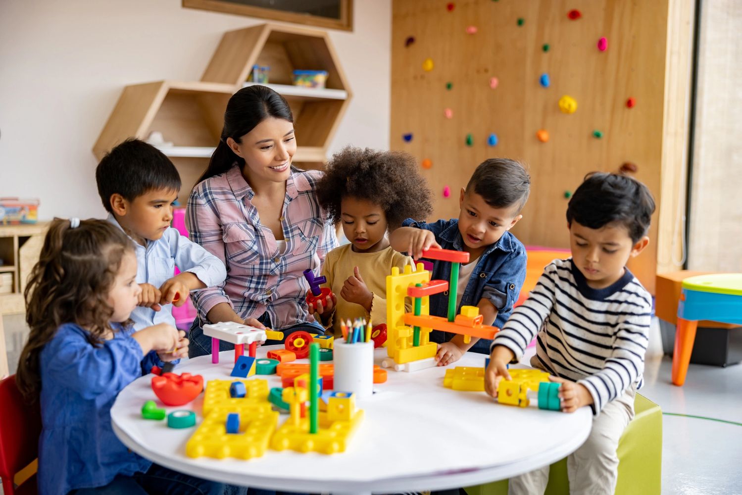 Teacher and diverse children playing with educational toys at a table.