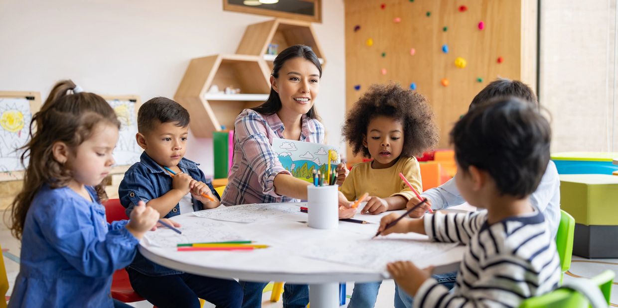 Image of a young lady seated at a round table with several children. They are coloring.