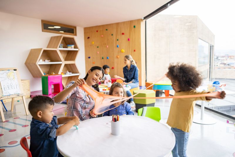 Happy Latin American teacher having fun with her students playing with slime at the school - elementary education concepts