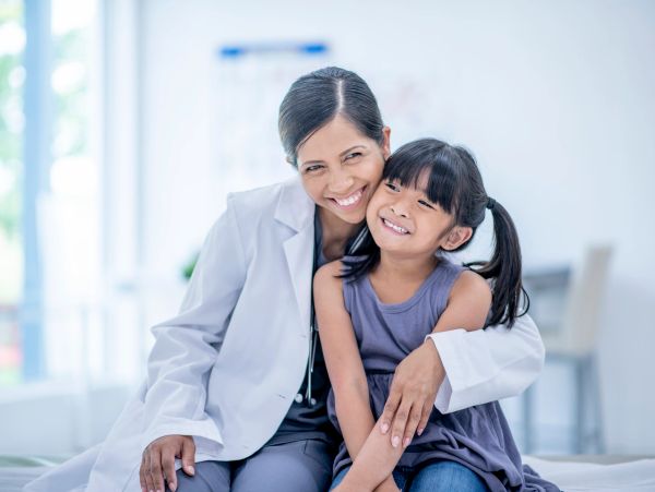 Smiling female doctor hugging a happy young girl.