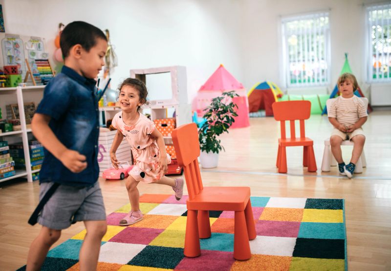 Smiling teacher and little child talking and playing at preschool