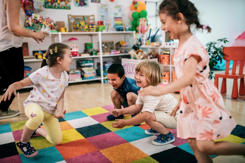 Smiling teacher and little child talking and playing at preschool