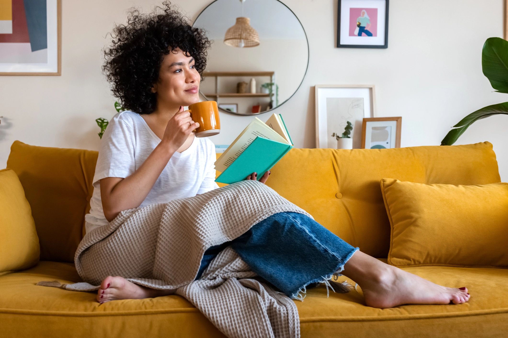 Woman relaxing on a yellow couch with a book and coffee.