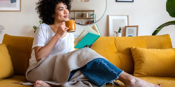 Woman relaxing on a mustard yellow sofa with a book and coffee.