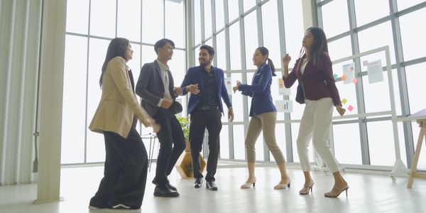 Five professionals dancing joyfully in a modern office space.