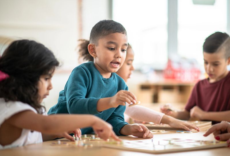 A diverse group of children work on a puzzle together at the table.