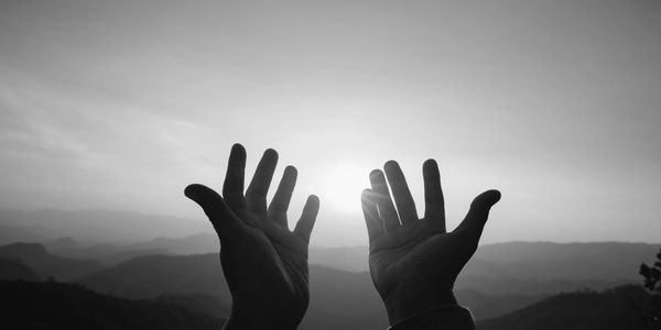 Silhouetted hands reaching towards the sun over mountain ranges.