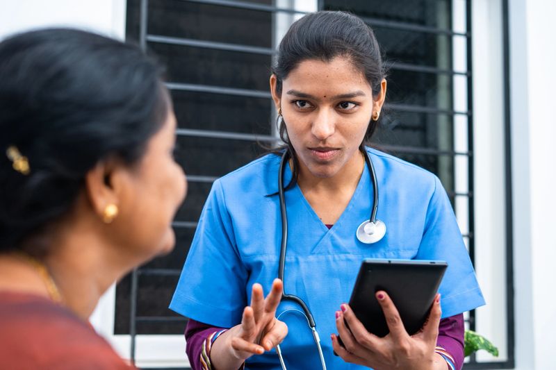 Doctor or nurse advising middle aged woman by seeing report from digital tablet at nursing home - concept of technology, healthcare and medical service.